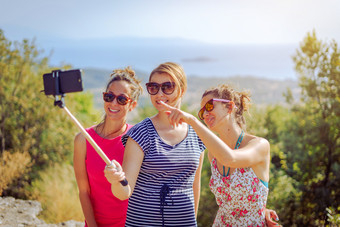 三个美丽的女孩女旅行者夏天礼服采取自拍与智能手机使用自拍坚持朋友友谊在户外的山以上的海秋天