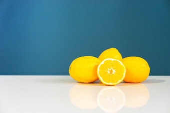 黄色的成熟的柠檬切片一半多汁的柑橘类水果的白色表格前面的蓝色的背景墙新鲜的水果