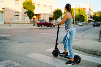 年轻的女人游乐设施电踢踏板车的街等待的十字路口穿牛仔裤夏天一天晚上<strong>交通运输</strong>