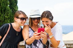 三个女人看的智能手机移动电话搜索为的旅游信息照片的科孚岛小镇