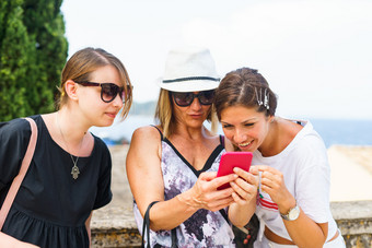 三个女人看的智能手机移动电话搜索为的旅游信息照片的科孚岛小镇