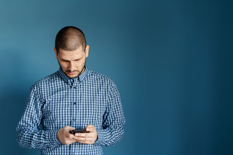 高加索人男人。穿衬衫站前面的蓝色的背景墙使用聪明的电话移动发送消息短信发短信浏览互联网前面视图