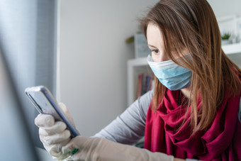 年轻的女人穿保护手套手和面具脸工作从首页办公室工作的表格移动PC移动电话发短信短信防止病毒传播疫情检疫预防