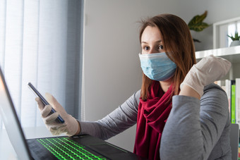 年轻的女人穿保护手套手和面具脸工作从首页办公室工作的表格移动PC移动电话防止病毒传播在疫情检疫预防