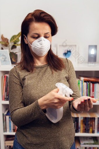 肖像成熟的高加索人女人穿抗菌保护面具在流感大流行站前面书架上工作首页防止疾病传播应用酒精消毒液手