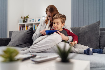 妈妈。和儿子年轻的女人和她的男孩孩子高加索人孩子坐着的沙发床上首页使视频调用玩视频游戏移动聪明的电话在检疫封锁