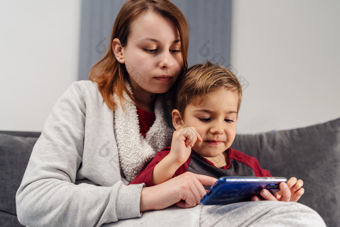 妈妈。和儿子年轻的女人和她的男孩孩子高加索人孩子坐着的沙发床上首页使视频调用玩视频游戏移动聪明的电话在检疫封锁