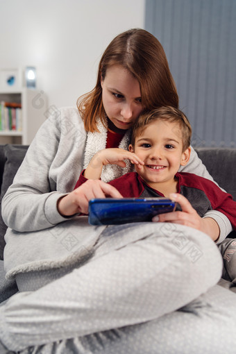妈妈。和儿子年轻的女人和她的男孩孩子高加索人孩子坐着的沙发床上首页使视频调用玩视频游戏移动聪明的电话在检疫封锁前面视图