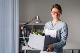 年轻的成人高加索人女人女女孩站的窗口的办公室失去她的工作持有个人项目的事情盒子被解雇了从工作驳回了由于危机经济衰退戒烟