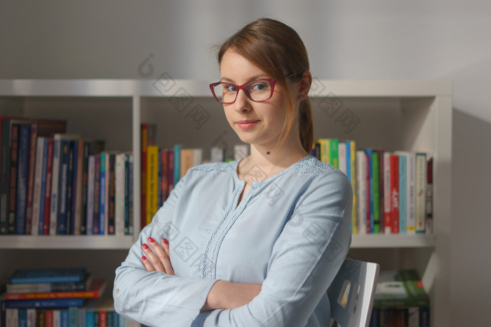 腰肖像年轻的高加索人女人成人女孩坐着的椅子首页办公室前面的书架子上穿眼镜和衬衫看的相机前面视图早....一天