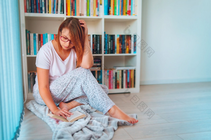 肖像年轻的成人高加索人女人女女孩前面的书架上首页在的周末假期坐着的地板上持有书阅读的架子上穿眼镜前面视图