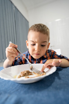 肖像小高加索人男孩小孩子孩子坐着的表格吃有午餐晚餐持有叉使脸手势前面视图首页