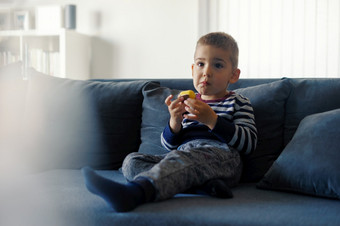 肖像一个小三个年老高加索人男孩小孩子孩子坐着的沙发床上<strong>首页</strong>持有巧克力<strong>糖果</strong>手吃而看前面视图
