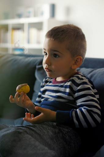 肖像一个小三个年老高加索人男孩小孩子孩子坐着的沙发床上首页持有巧克力糖果手吃而看一边视图