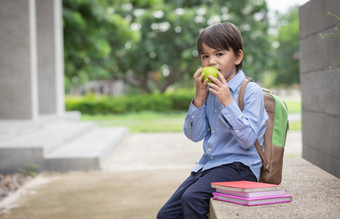 可爱的小男孩穿<strong>蓝色</strong>的衬衫和携带学生背包收到苹果从妈妈。为早餐之前学校早餐重要的为孩子发展<strong>健康</strong>和<strong>健康</strong>