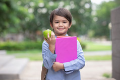 可爱的小男孩穿蓝色的衬衫和携带学生背包收到苹果从妈妈。为早餐之前学校早餐重要的为孩子发展健康和健康