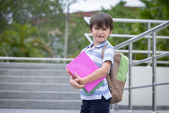 微笑可爱的小男孩与学校背包和持有书准备好了为第一个一天学校