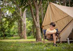 可爱的男孩坐着专心地阅读书前面帐篷在野营