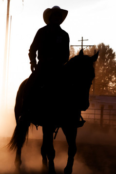 日落轮廓马回来骑手发光马术牛仔竞技表演尘土飞扬的竞技场骑