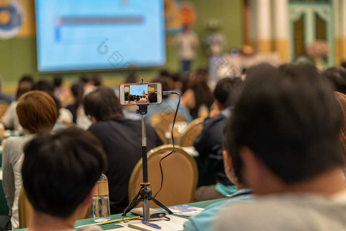 特写镜头聪明的移动电话采取生活流媒体与观众亚洲演讲者与休闲西装站和给的知识的阶段的会议大厅研讨会会议业务和教育概念