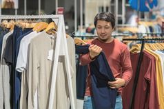 聪明的亚洲男人。与胡子选择衣服服装商店购物中心看色彩斑斓的t-sshirts时尚和消费主义概念