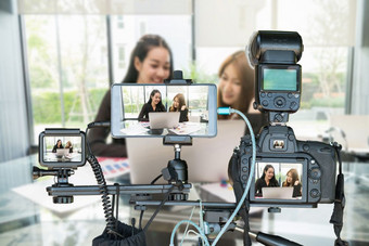 专业集相机与聪明的移动电话和行动相机三脚架在两个亚洲年轻的女商人给的面试通过生活流生活流媒体为企业家概念