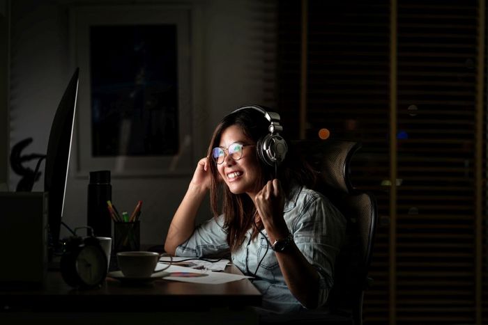 肖像亚洲女商人听的音乐通过耳机和聪明的移动电话与很高兴行动的表格工作场所晚些时候时间工作硬和太晚些时候概念
