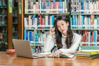 亚洲年轻的学生休闲西装思考当做家庭作业和使用技术移动PC图书馆<strong>大学通知书</strong>的与各种各样的书和静止的在的书架子上回来学校