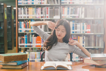 亚洲年轻的学生<strong>休闲西装</strong>阅读和做拉伸自己图书馆大学通知书的与各种各样的书和静止的的木表格在的书架子上回来学校
