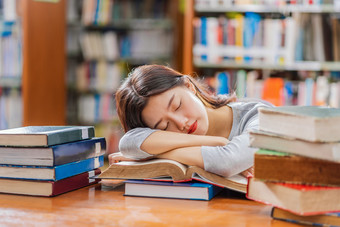 亚洲年轻的学生休闲西装阅读和睡觉的木表格与各种各样的书图书馆大学通知书的在的书架子上回来学校概念