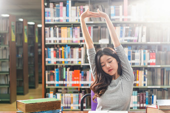 亚洲年轻的学生休闲西装阅读和做<strong>拉伸</strong>自己图书馆大学通知书的与各种各样的书和静止的的木表格在的书架子上回来学校