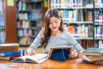 亚洲年轻的学生休闲西装做家庭作业和使用技术特布莱特图书馆大学通知书的与各种各样的书和静止的在的书架子上背景回来学校