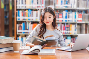 亚洲年轻的学生休闲西装做家庭作业和使用技术移动PC图书馆大学通知书的与各种各样的书和静止的在的书架子上背景回来学校