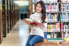 亚洲年轻的学生休闲西装阅读的书图书馆大学通知书的的木表格在的书架子上背景回来学校概念