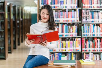 亚洲年轻的学生休闲西装阅读的书图书馆大学通知书的的木表格在的书架子上背景回来学校概念