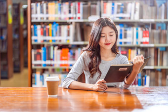 亚洲年轻的学生休闲西装阅读的书与杯咖啡图书馆大学通知书的的木表格在的书架子上背景回来学校概念