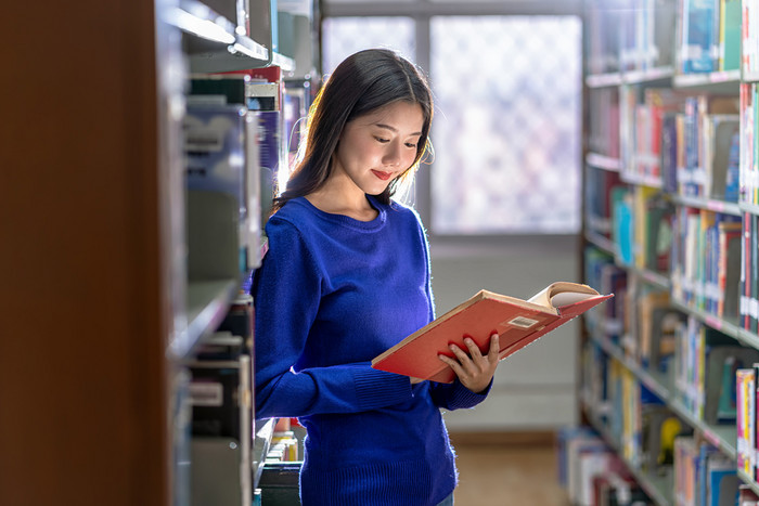 亚洲年轻的学生休闲西装站和阅读的书书架子上图书馆大学通知书的与各种各样的书背景回来学校概念