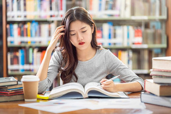 亚洲年轻的学生休闲西装阅读和做家庭作业图书馆大学通知书的与各种各样的书和静止的的木表格在的书架子上背景回来学校