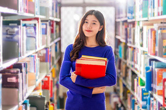 亚洲年轻的学生休闲西装持有后搜索的书从书架子上图书馆大学通知书的与各种各样的书背景回来学校概念