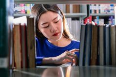 亚洲年轻的学生休闲西装搜索的书严重的感觉从书架子上图书馆大学通知书的与各种各样的书背景回来学校概念