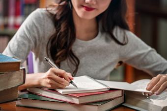 特写镜头亚洲年轻的学生手写作家庭作业图书馆大学通知书的与各种各样的书和静止的与咖啡杯木表格在的书架子上背景回来学校