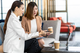 两个亚洲女商人讨论与的<strong>合作伙伴</strong>业务与技术移动PC在咖啡打破现代办公室共同办公空间咖啡打破放松和会说话的<strong>合作伙伴</strong>和的同事