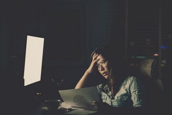 肖像亚洲女商人坐着和工作硬的表格与前面电脑桌面工作场所晚些时候与严重的行动工作硬和太晚些时候概念