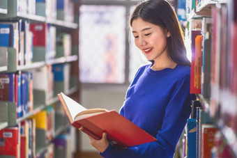 亚洲年轻的学生休闲西装站和阅读的书书架子上图书馆大学通知书的与各种各样的书背景回来学校概念