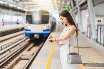 年轻的亚洲女人乘客听音乐通过聪明的移动<strong>电话</strong>和看火车与手看<strong>地铁</strong>火车站日本中国人朝鲜文生活方式通勤和运输概念
