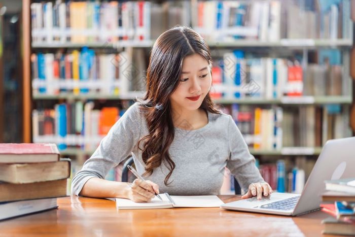 亚洲年轻的学生休闲西装做家庭作业和使用技术移动PC图书馆大学通知书的与各种各样的书和静止的在的书架子上背景回来学校