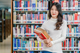 肖像亚洲年轻的学生休闲西装站和持有的书书架子上图书馆大学通知书的与各种各样的书背景回来学校概念