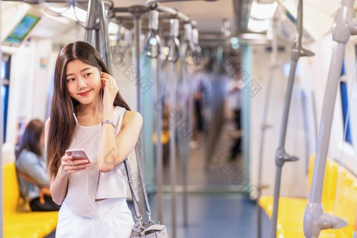 年轻的亚洲女人乘客听音乐通过聪明的移动电话地铁火车当旅行大城市日本中国人朝鲜文生活方式和每天生活通勤和运输概念