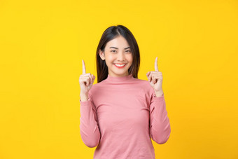 亚洲微笑年轻的女人手指指出为做<strong>广告</strong>横幅显示孤立的黄色的颜色背景穿冬天舒适的毛衣在<strong>室内</strong>工作室幸福和有趣的复制空间概念