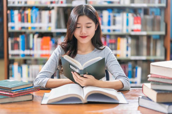 亚洲年轻的学生休闲西装阅读的书的木表格图书馆大学通知书的与各种各样的书和静止的在的书架子上背景回来学校概念